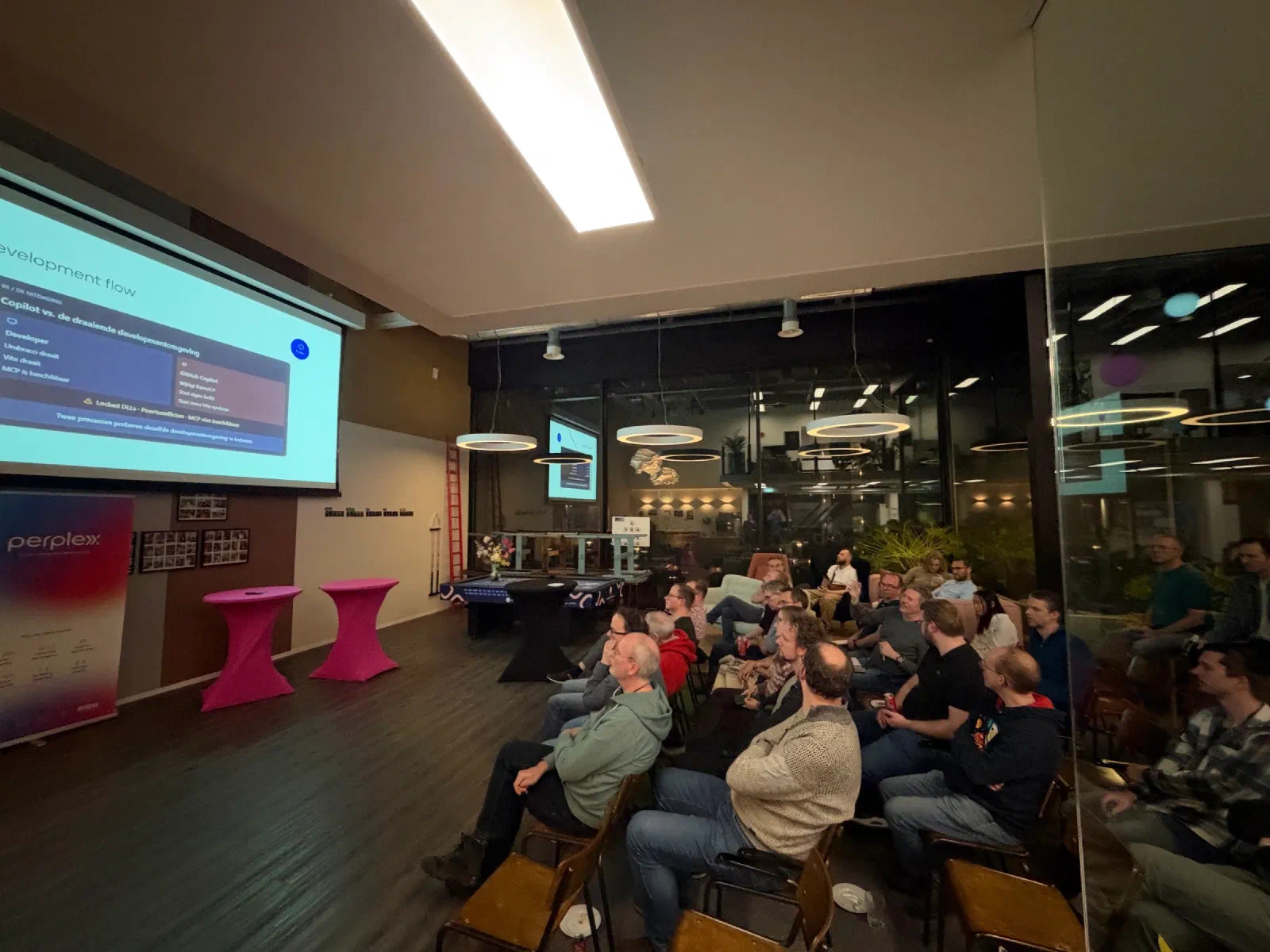Een volle zaal kijkt naar een groot scherm met een dia over de developmentflow